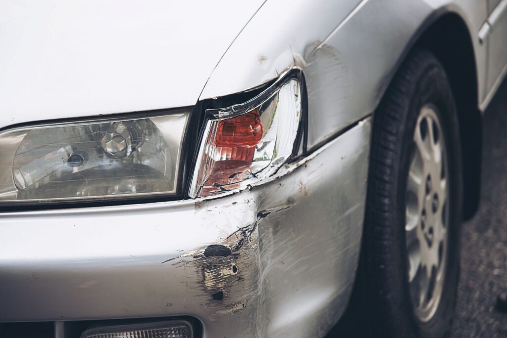 A silver car was involved in a minor collision, leaving visible damage at the front left side of the car. 