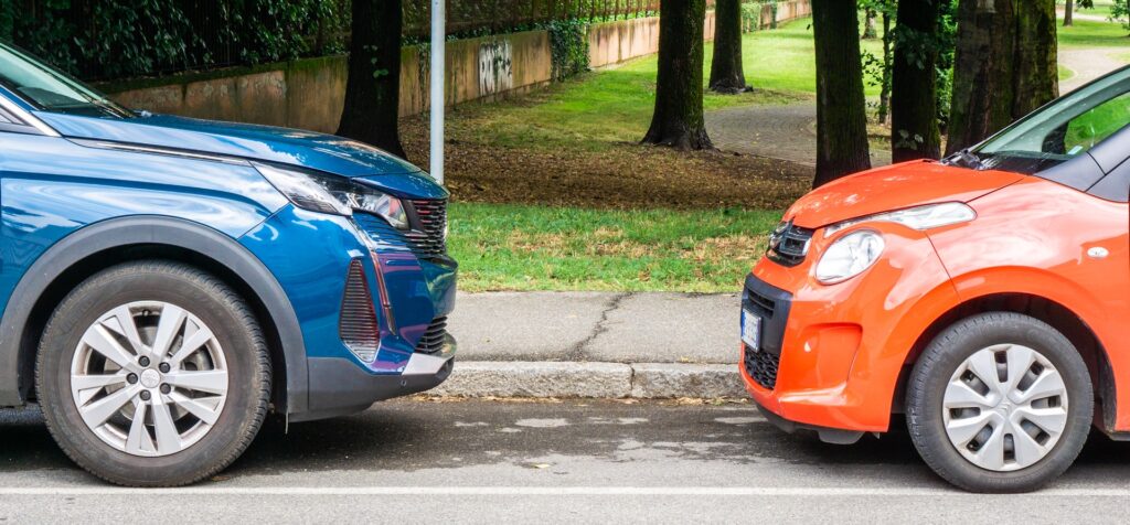 A blue car and a orange car parked at the roadside.