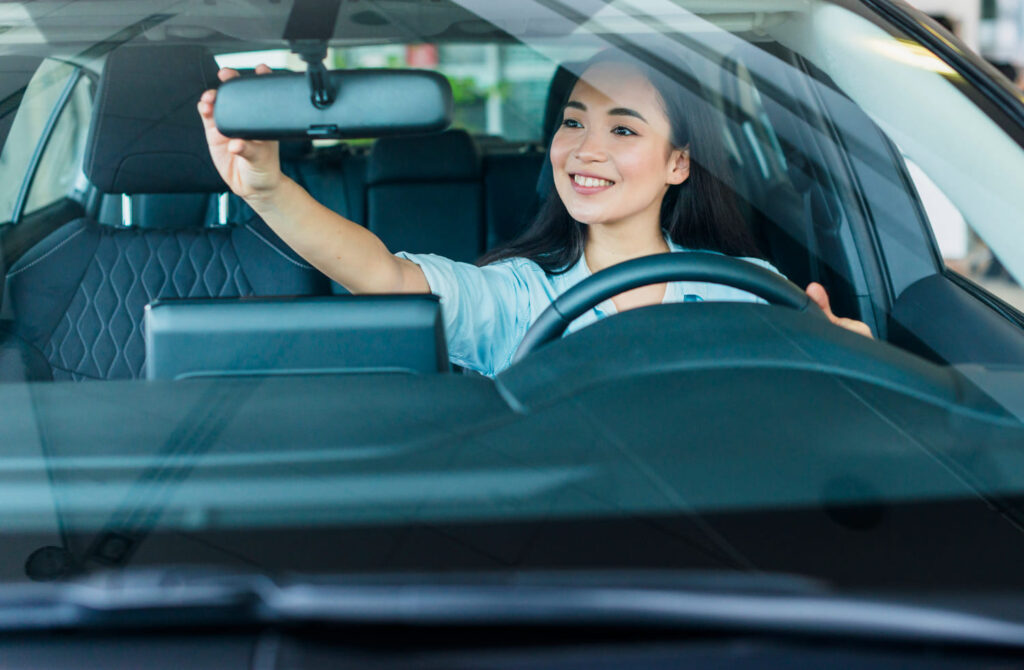 A woman adjusts rear-view mirror. 