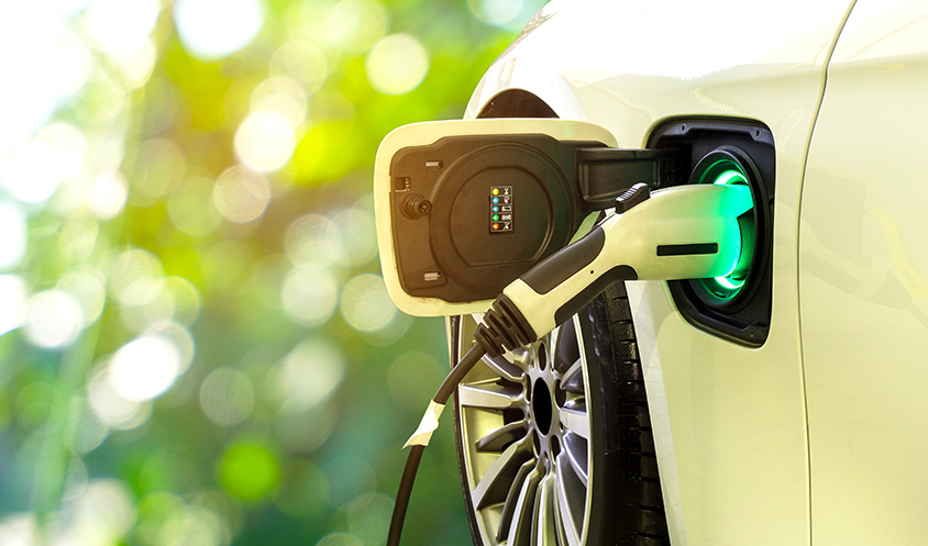 EV Car or Electric car at charging station with the power cable supply plugged in on blurred nature with soft light background. Eco-friendly alternative energy concept